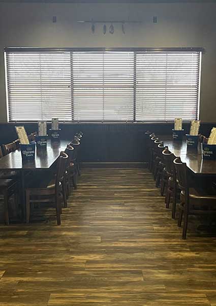 Spacious banquet room Monticello MN with two long tables, wooden chairs, and closed blinds.