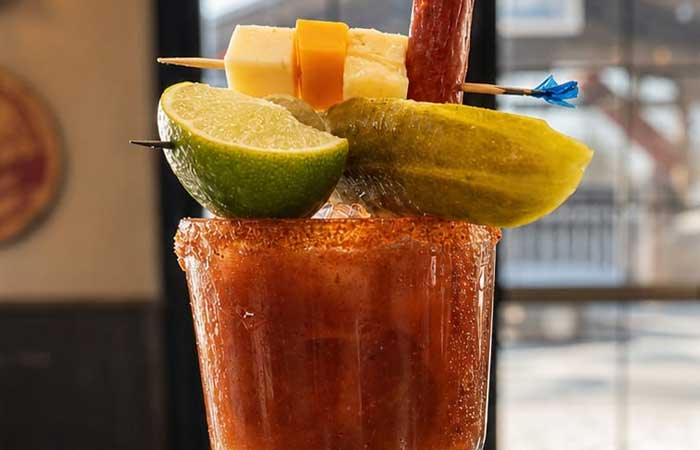 Bar menu Monticello MN: Bloody Mary garnished with lime, pickle, cheese cubes, and meat stick.