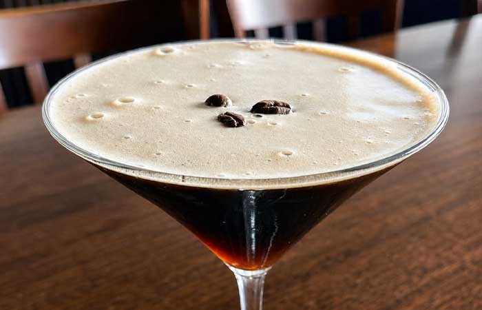 A dark espresso martini in a glass, featured on the Bar menu Monticello MN, with coffee beans.