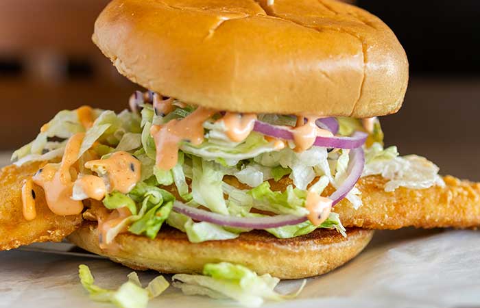 Featured on our restaurant menu Monticello MN: fish sandwich with lettuce, onions, and sauce.