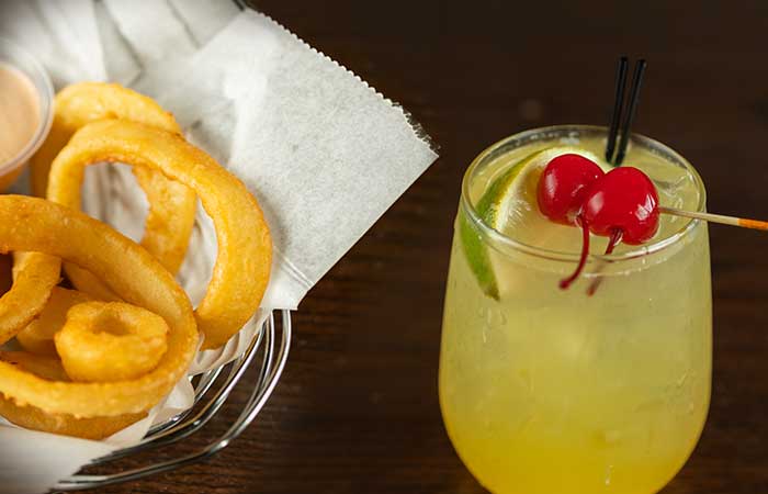 Curly fries in a basket beside a yellow Monticello restaurant drink garnished with lime, cherries.