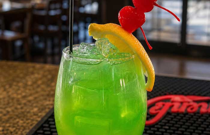 On our Bar menu Monticello MN: Bright green cocktail with ice, orange slice, and two cherries.