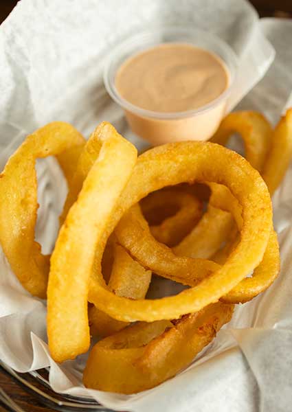 Golden onion rings in a basket with dipping sauce, perfect at any restaurant in Monticello MN.