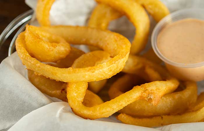 Golden onion rings in a basket, perfect for happy hour in Monticello MN with dipping sauce.