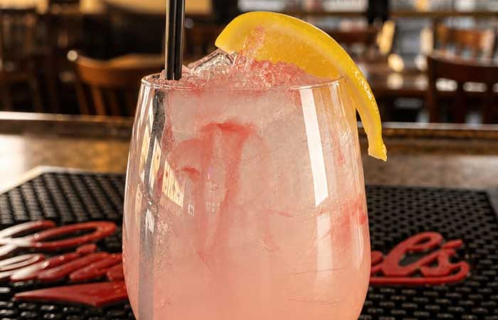 A pink cocktail with ice, lemon, and straw sits on a Bar menu Monticello MN counter.