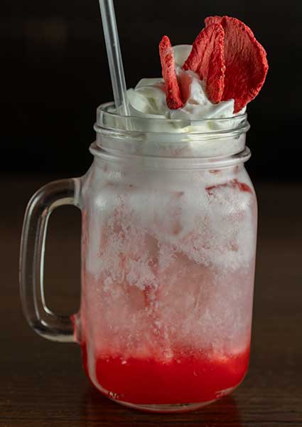 A mason jar from a restaurant in Monticello MN holds red icy drink, whipped cream, and a straw.