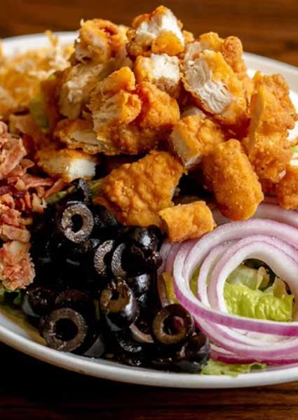 A salad with breaded chicken, olives, bacon, and onion served at a restaurant in Monticello, MN.