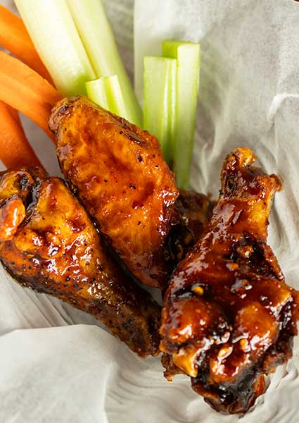Three glazed chicken wings with carrot and celery sticks at a restaurant in Monticello, MN.