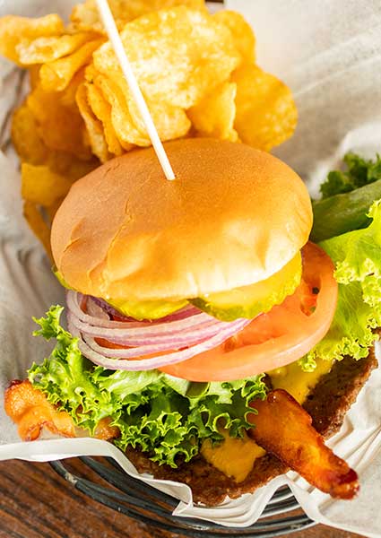 A cheeseburger with bacon, lettuce, tomato, and chips at a restaurant in Monticello, MN.