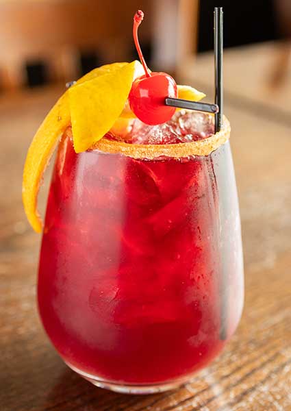 Red cocktail garnished with an orange slice and maraschino cherry at a restaurant in Monticello MN.